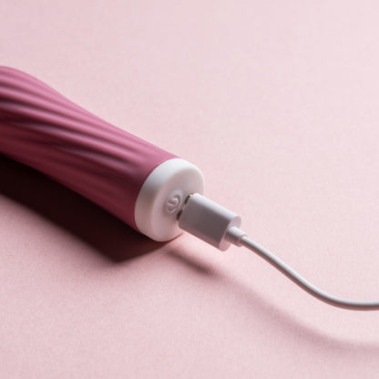 Pink bullet vibrator with charging lead inserted on pink background

