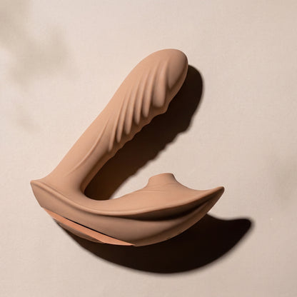 Bronze clitoral suction vibrator laying on it's side on a beige background
