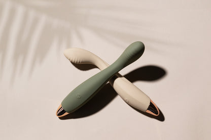 Vanilla G-spot vibrator laying down with green vibrator resting on it, palm leaf shadow in background