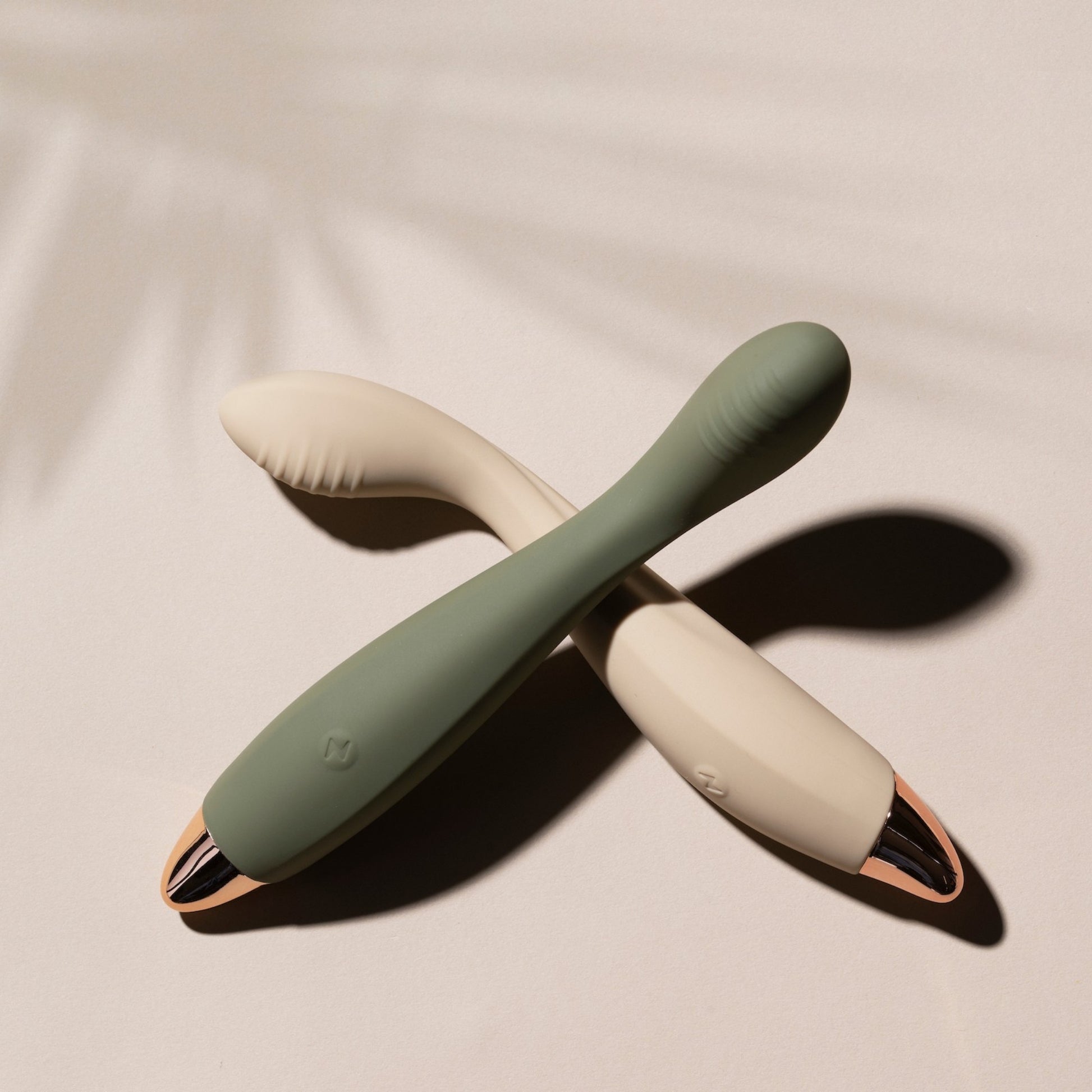 Two green and vanilla G-spot vibrators on a beige background