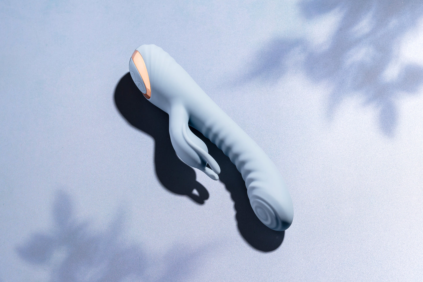Blue rabbit vibrator laying on blue surface with soft tree shadows