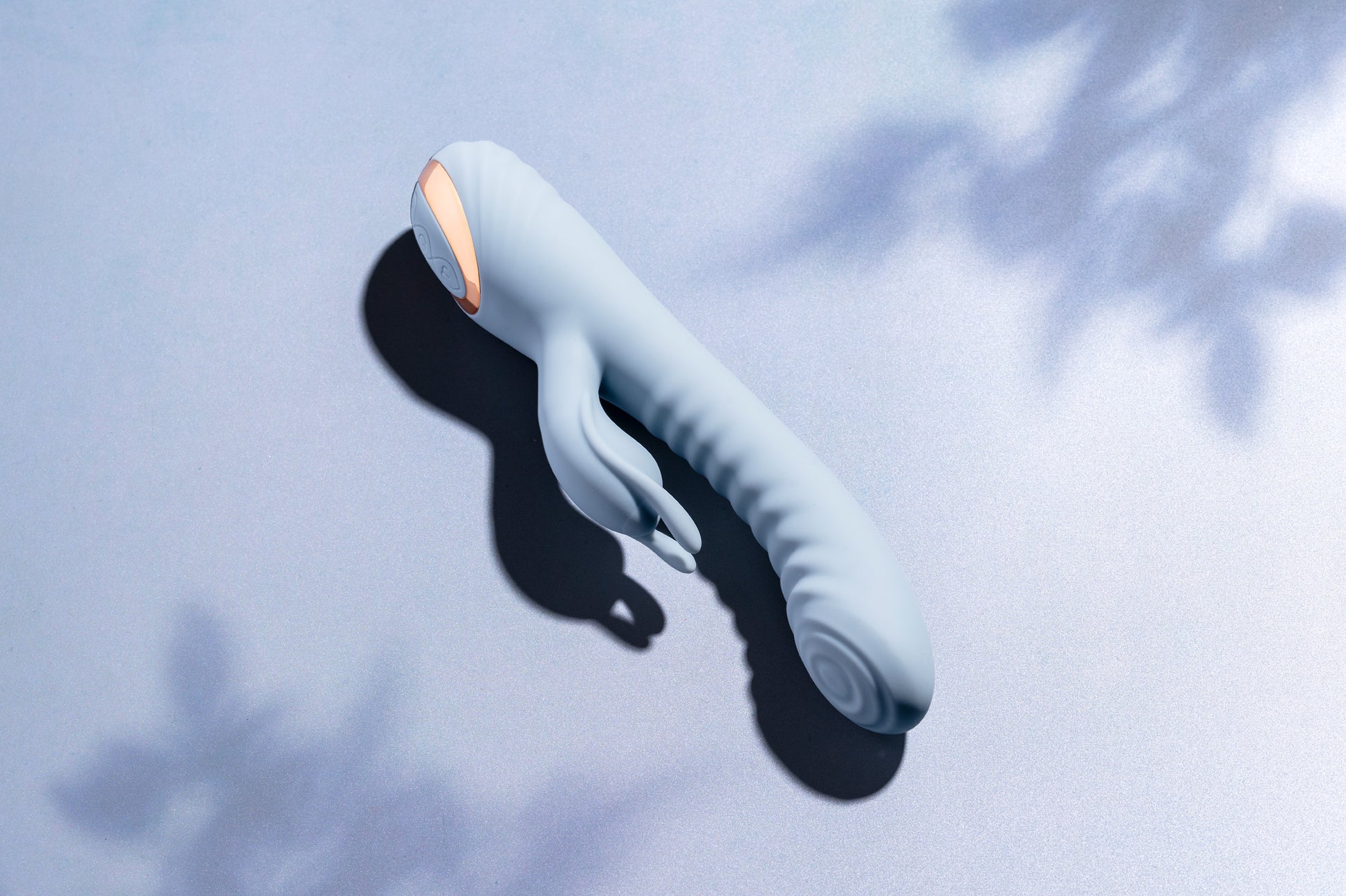 Blue rabbit vibrator laying on blue surface with soft tree shadows