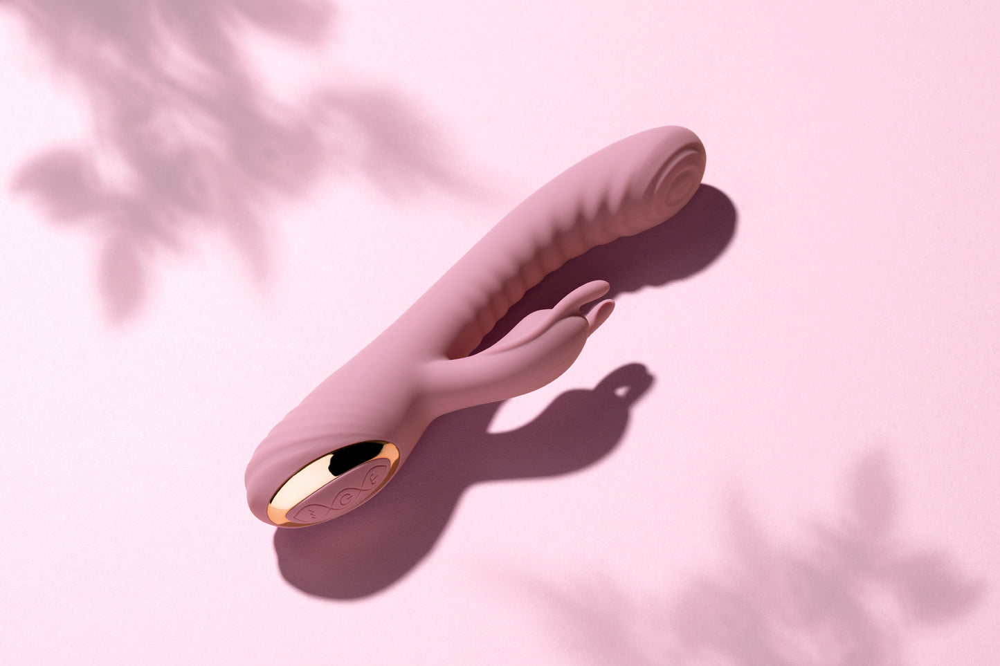 Pink rabbit vibrator laying on pink surface with gentle tree shadows