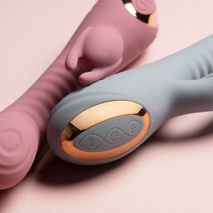 Close-up of control buttons on pink and blue rabbit vibrators laying side by side, pink background

