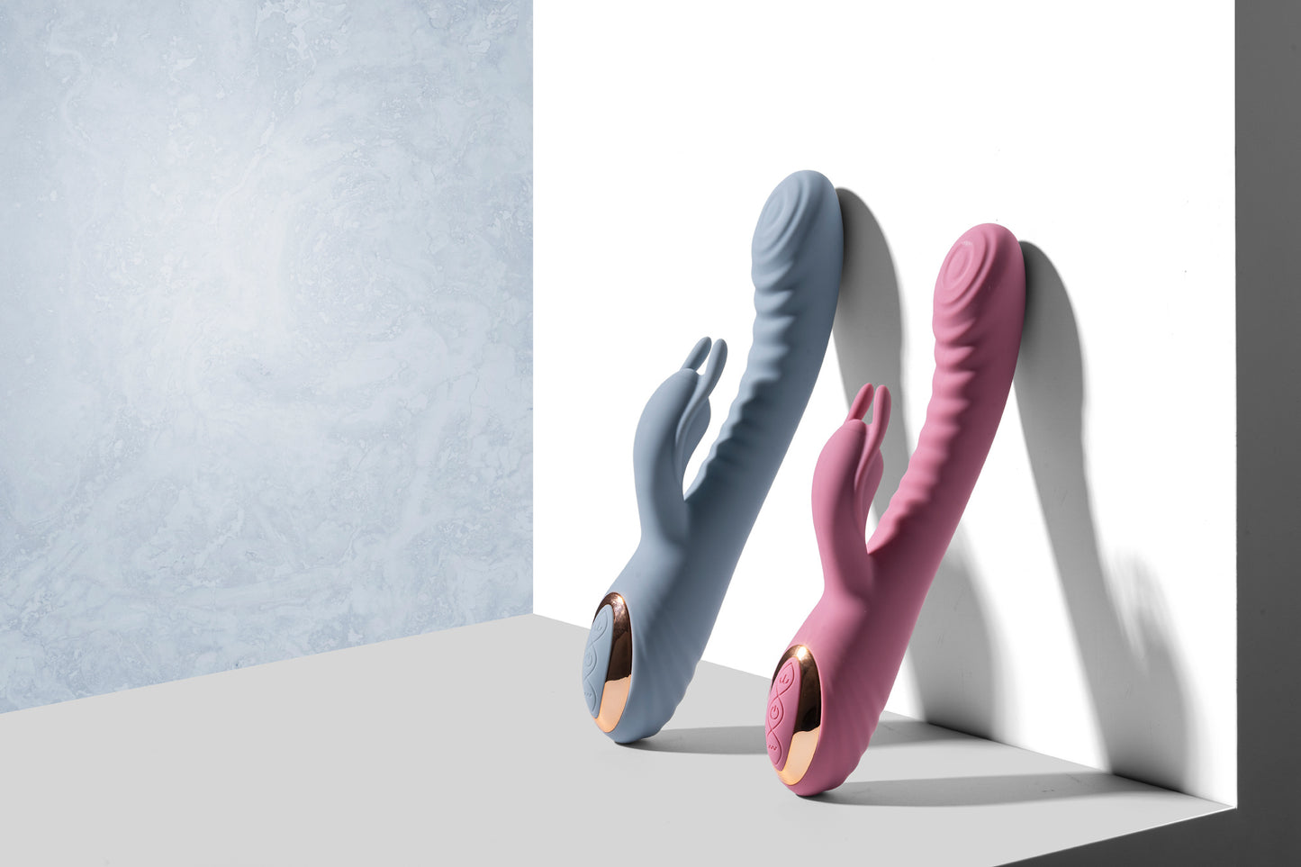 Pink and blue rabbit vibrators standing upright on grey surface against white backdrop