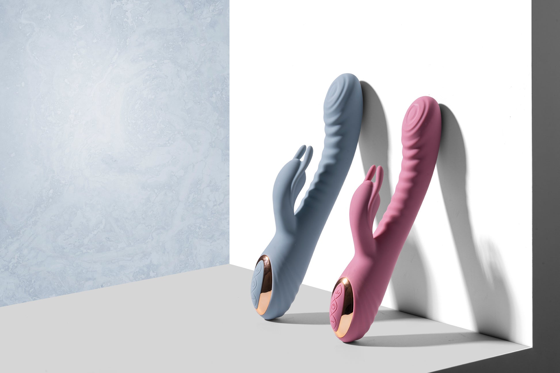 Pink and blue rabbit vibrators standing upright on grey surface against white backdrop