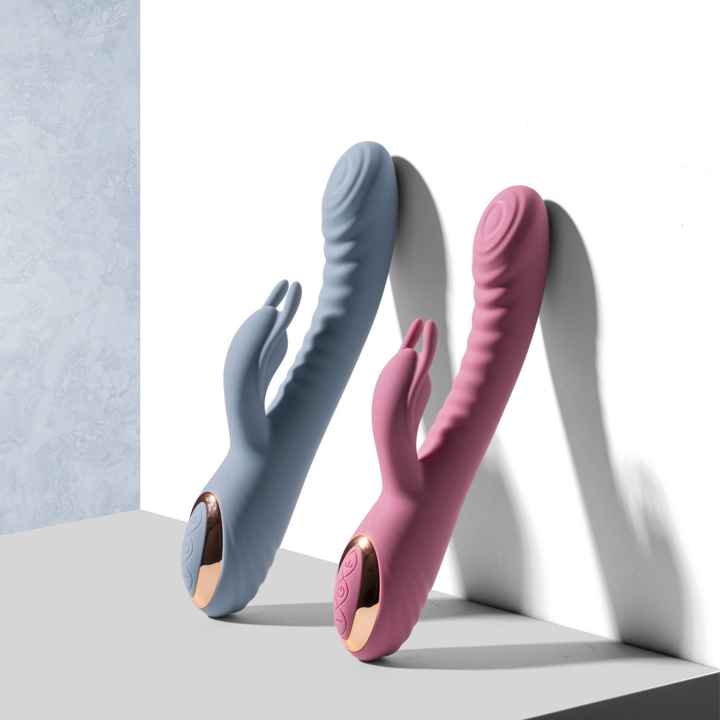 Two rabbit vibrators, one blue and one pink, on a light gray surface with a white background.